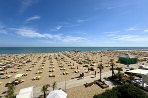 A beach with numerous sun loungers and umbrellas, a clear sky, and a calm sea.