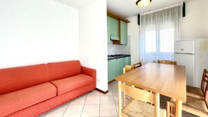 Un espacio habitable compacto con un sofá rojo, una mesa de comedor de madera y sillas. Se ve una cocina con armarios verdes y un refrigerador blanco al fondo.