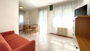 Una sala de estar con sofá, una mesa de comedor con sillas, televisión y radiador.