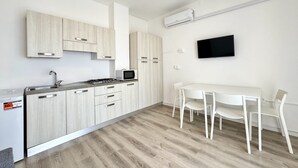 A modern kitchen with light wood cabinets, a built-in microwave, and a dining area with a white table and chairs.