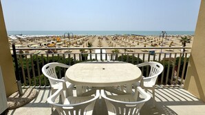 A balcony with a table and chairs overlooking a beach with umbrellas and sun loungers.