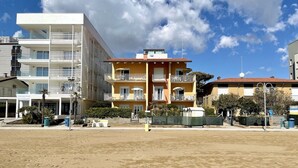A beachfront hotel with multiple balconies, a sandy beach in front, and a clear sky.