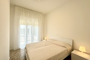 Une chambre d’hôtel avec un grand lit, deux tables de chevet avec des lampes, une fenêtre avec des rideaux légers et une vue sur l’extérieur.