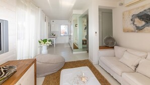 A modern living room with a sofa, a coffee table, and a TV. There is a kitchen in the background with a dining area.