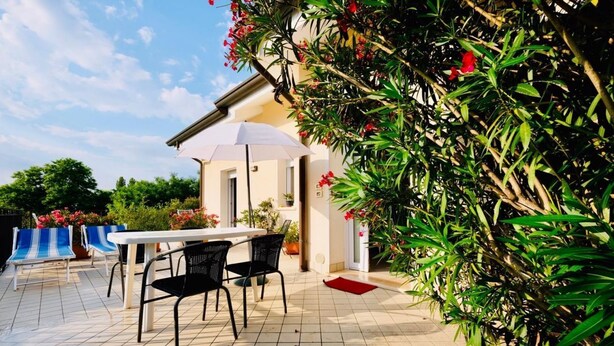 Eine Terrasse im Freien mit Tisch, Stühlen, einem weißen Sonnenschirm und üppigem Grün.