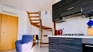 Eine moderne Küche mit dunklen Schränken, einem Gasherd und einem eingebauten Ofen. Eine Holztreppe führt auf eine obere Ebene.