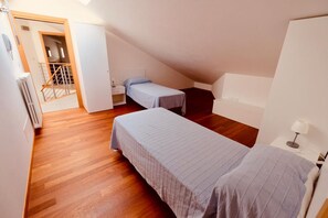 Een klein appartement met één kamer, twee bedden, een houten vloer, een radiator, een bureau en een stoel.