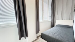 A bedroom with a bed, a window with blinds, and curtains.