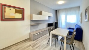 A modern living room with a dining table, chairs, a TV, and a sofa.