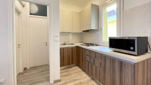 A compact kitchen with wooden cabinets, a gas stove, a microwave, and a window providing natural light.