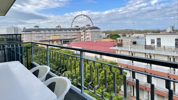 A balcony with a view of a Ferris wheel, residential buildings, and a red-roofed structure.
