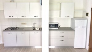 A modern kitchen with white cabinets, a gas stove, a sink, a microwave, and a refrigerator. - Appartamento Villa Santin 4-Carraro Immobiliare Jesolo (Lido di Jesolo)