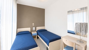 Une chambre avec deux lits simples, un bureau, une chaise, un miroir et une fenêtre avec des rideaux.