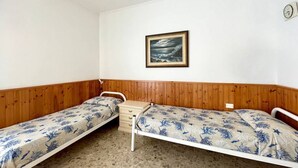 Een kleine kamer met twee eenpersoonsbedden, een houten paneelwand, een lijst met een afbeelding en een klein houten dressoir.