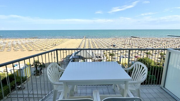 Een balkon met een tafel en stoelen, met uitzicht op een strand met rijen ligbedden.