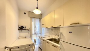Una cocina compacta con armarios blancos, un lavamanos, un refrigerador y un microondas.