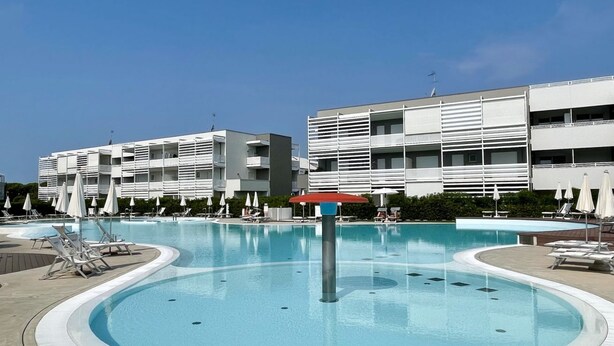 Une piscine entourée de bâtiments modernes dotés de balcons, avec des chaises longues et des parasols à proximité.