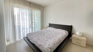 Une chambre à coucher avec un lit, une table de chevet, une lampe et une fenêtre avec des rideaux.