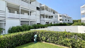 Un immeuble résidentiel moderne à plusieurs étages, doté de balcons, d’une pelouse verdoyante et d’un élément décoratif aquatique.