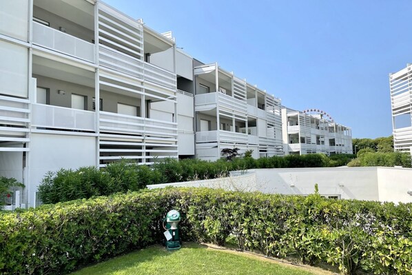 A modern multi-story residential building with balconies, a green lawn, and a water feature.
