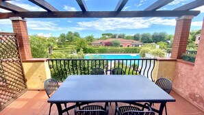 Un espace extérieur abrité, doté d’une table et de chaises, qui offre une vue sur une piscine et un jardin luxuriant.