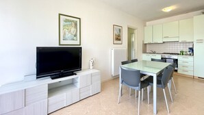 Une cuisine moderne avec des meubles blancs, une table à manger avec des chaises, un téléviseur à écran plat posé sur un meuble blanc et des tableaux encadrés accrochés au mur.