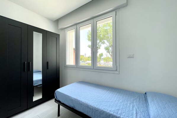 Un dormitorio con cama, armario y ventana con vistas a árboles y un edificio.