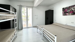 A room with bunk beds, a large bed, a sliding glass door to a balcony, and a black wardrobe. - DB1 Appartamento 8 posti letto Carraro Immobiliare Jesolo (Lido di Jesolo)