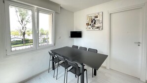A room with a large table and chairs, a flat-screen TV mounted on the wall, and a door. - DB1 Appartamento 8 posti letto Carraro Immobiliare Jesolo (Lido di Jesolo)