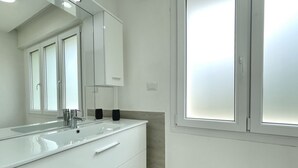 A modern bathroom with a large mirror, white vanity, and a window with frosted glass. - DB1 Appartamento 8 posti letto Carraro Immobiliare Jesolo (Lido di Jesolo)