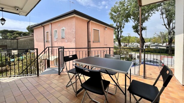 A balcony with a table and chairs, a peach-colored building in the background, and a clear sky. - DB1 Appartamento 8 posti letto Carraro Immobiliare Jesolo (Lido di Jesolo)