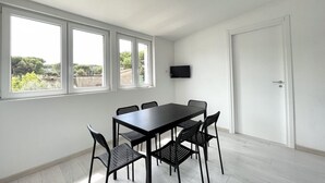 Quarto com uma janela grande, televisão de tela plana na parede e uma mesa de jantar com cadeiras.