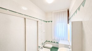 A bathroom with a shower, two toilets, a bidet, and a sink.
