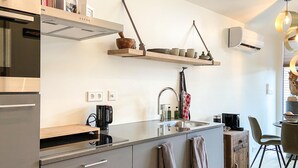 A modern kitchen with a built-in stove, a sink, and a wooden shelf above the counter. There are two power outlets on the wall and a coffee machine on the counter. - Stunning house in Spakenburg (Spakenburg)