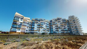 A modern multi-story residential building with balconies, a sandy foreground, and a clear blue sky. - Panoramic View face Mer (Saint-Gilles-Croix-de-Vie)