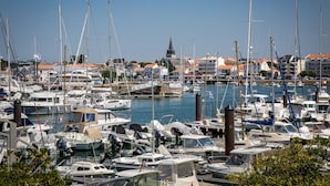 A marina with numerous boats docked, surrounded by buildings with red-tiled roofs. - Panoramic View face Mer (Saint-Gilles-Croix-de-Vie)