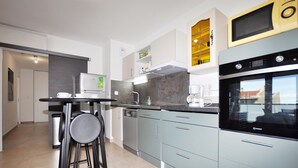 A modern kitchen with grey cabinets, a black oven, and a coffee machine. There is a small dining area with a table and two stools. - Stunning apartment in Canet en Roussillon (Canet en Roussillon)