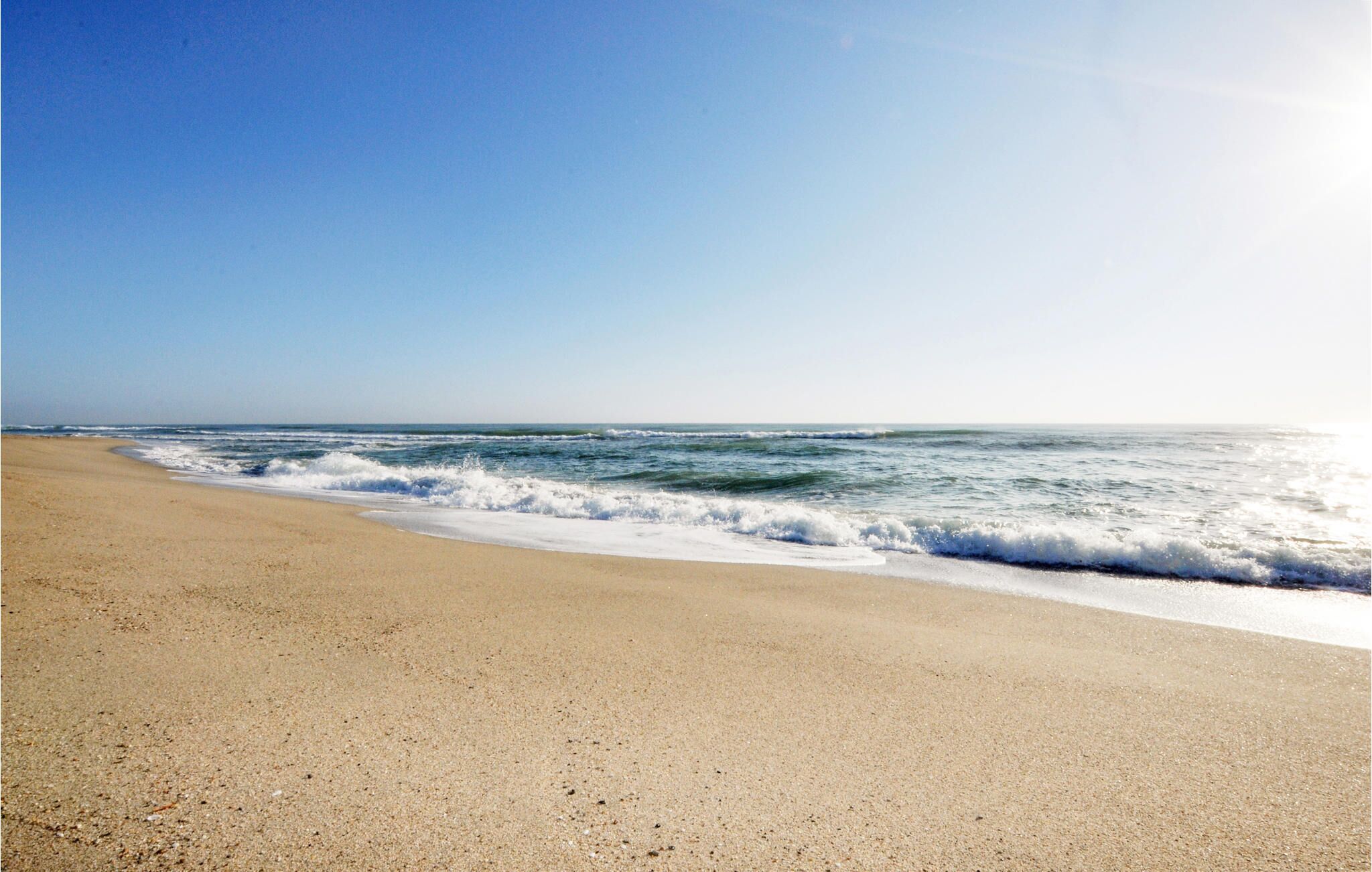 Une plage avec un ciel dégagé et des vagues.