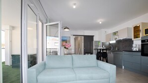 A modern living room with a light blue sofa, a dining area with a table and chairs, and a kitchen with grey cabinets and stainless steel appliances. - Stunning apartment in Canet en Roussillon (Canet en Roussillon)