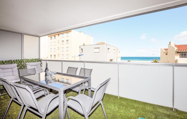 A balcony with a glass table and chairs, overlooking a beach and buildings.