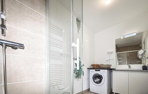 A compact bathroom with a glass shower enclosure, a washing machine, and a mirror.