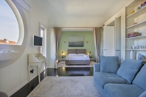 A modern hotel room with a bed, a TV, a sofa, and a view of the city.