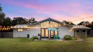 A single-story house with a large glass door, a patio with a table and chairs, and string lights.