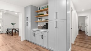 A modern kitchen with grey cabinets, wooden shelves, and a dining area with a table and chairs.