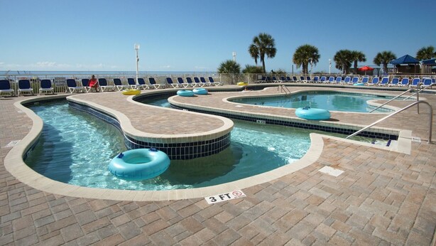 A pool area with multiple hot tubs and lounge chairs, a sign indicating no diving, and a clear view of the ocean. - Tropical oceanfront resort with shops, restaurants, pools, lazy river-paradise! Sleeps 4. (North Myrtle Beach)