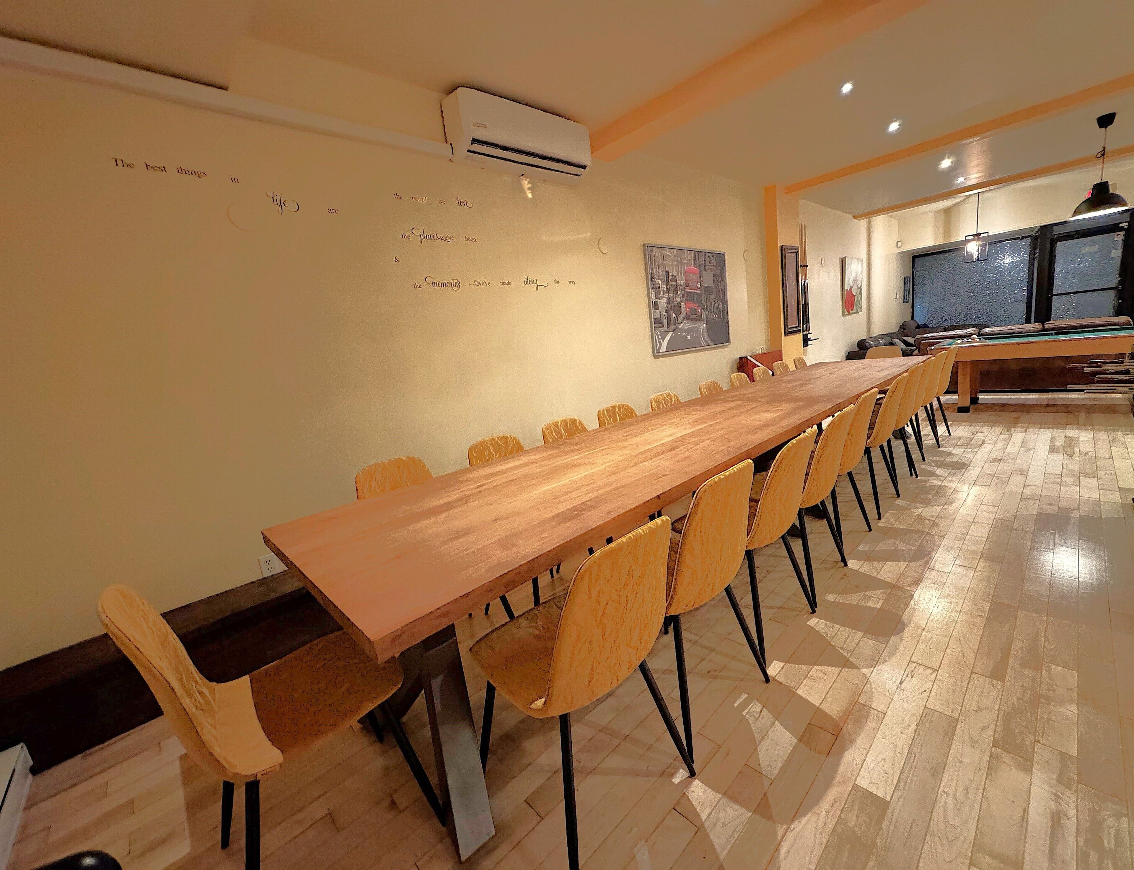 A long wooden table with chairs, an air conditioning unit, and a pool table in a room with tiled flooring.
