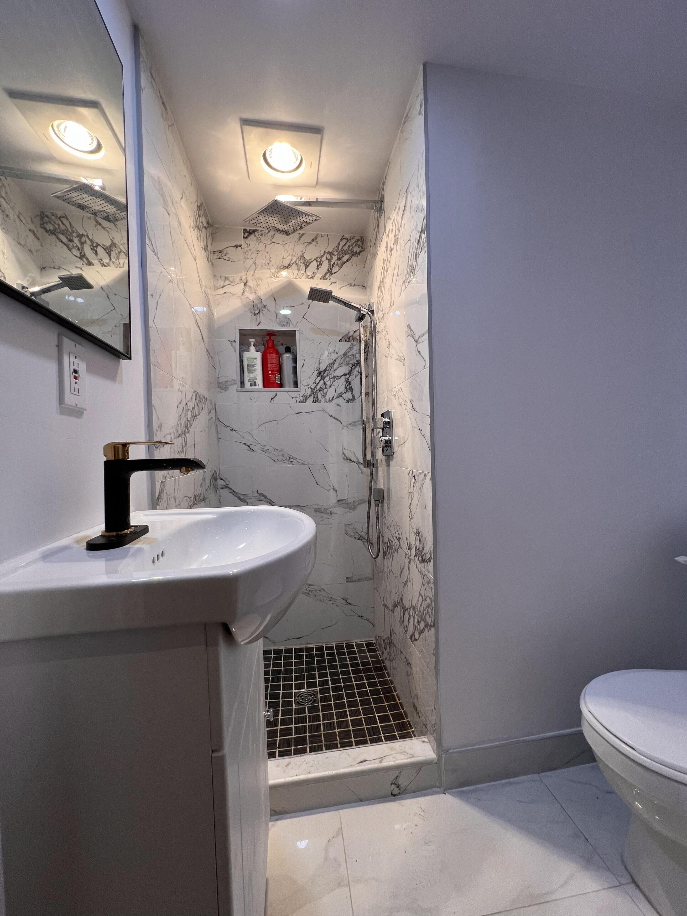 Une salle de bain avec un lavabo blanc, des toilettes, une douche avec une porte en verre et un miroir.