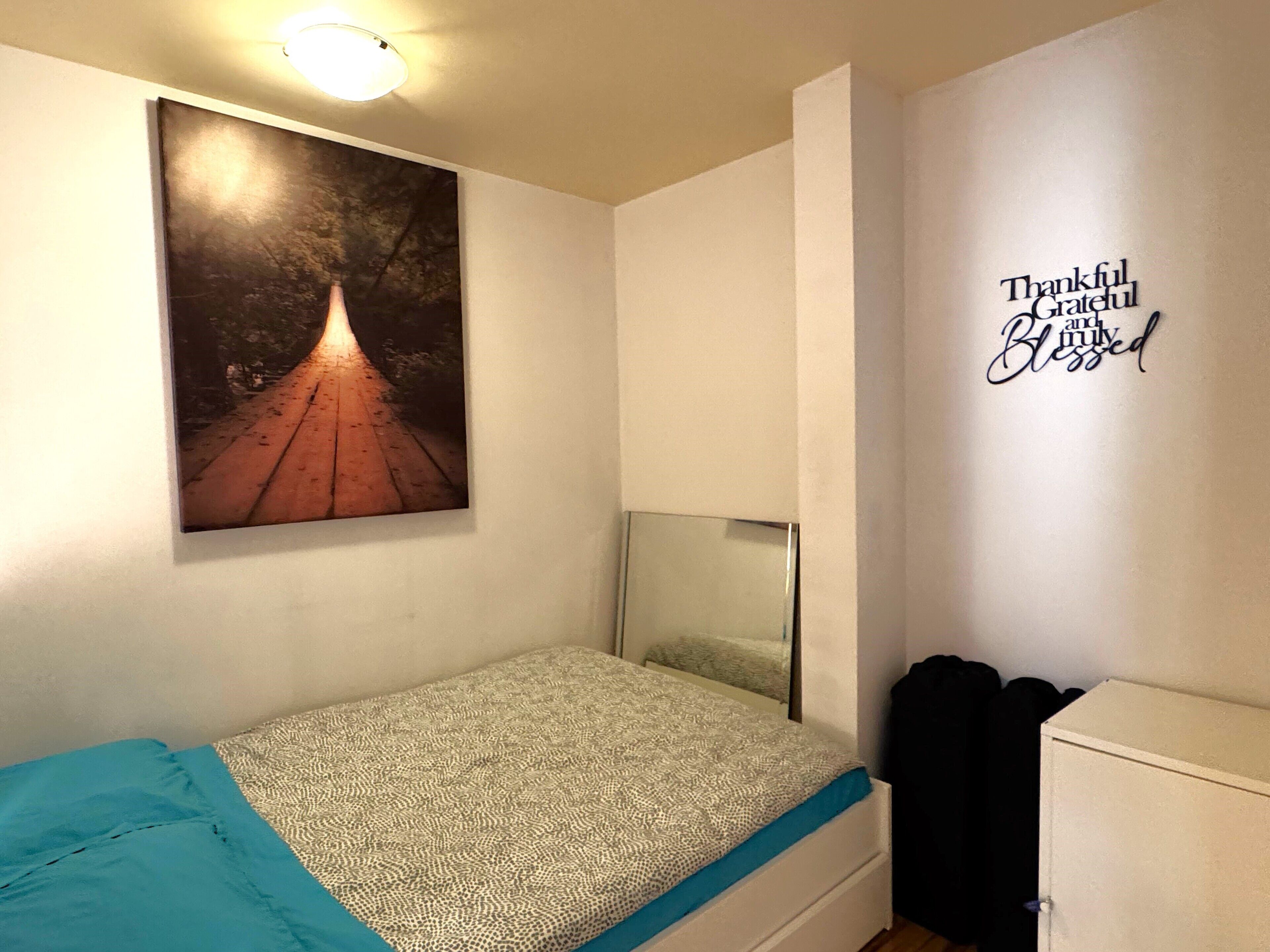 A bedroom with a bed, a wall-mounted picture, and a motivational quote.