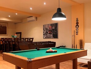 Ett biljardbord i ett rum med en matplats, en tavla och en väggmonterad luftkonditioneringsanläggning.