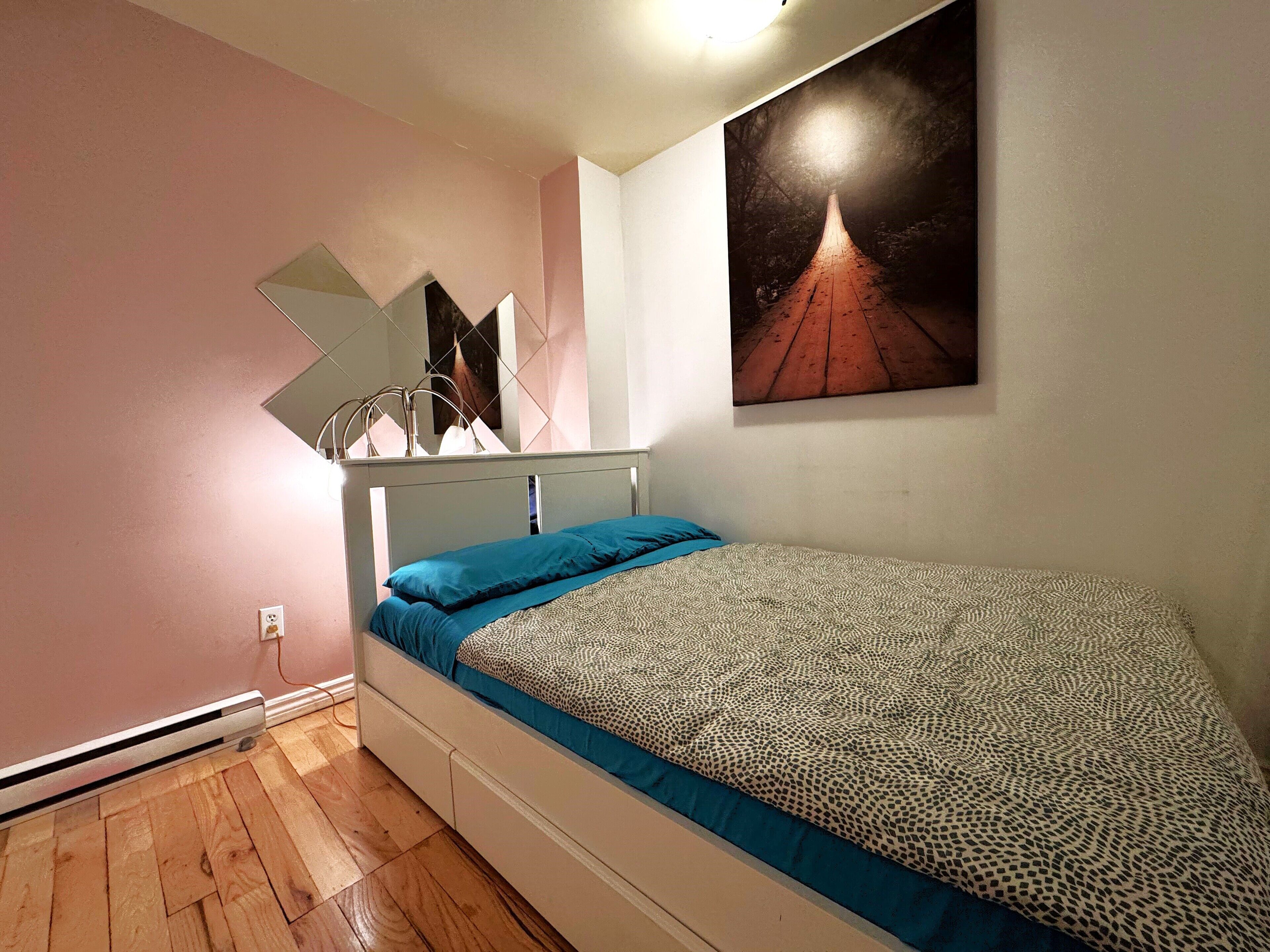 A bedroom with a bed, a wall-mounted lamp, and a painting.